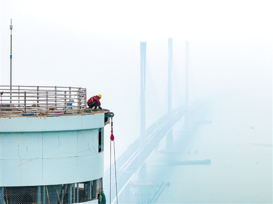 建設者在塔柱上施工，遠處“海上長龍”若隱若現(xiàn)。