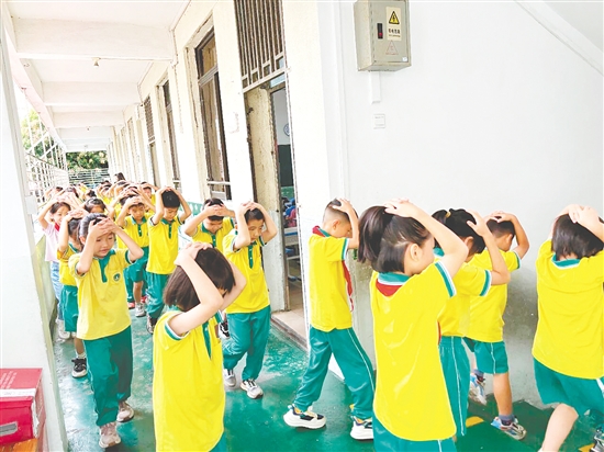 演練中，學(xué)生雙手抱頭、緊貼墻角，按照指定的逃生路線快速有序地撤離至操場(chǎng)安全區(qū)域。